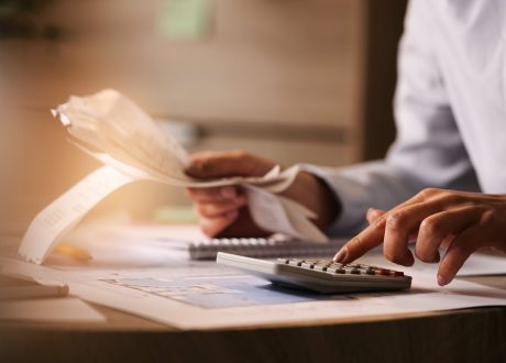 closeup-economist-using-calculator-while-going-through-bills-taxes-office-min